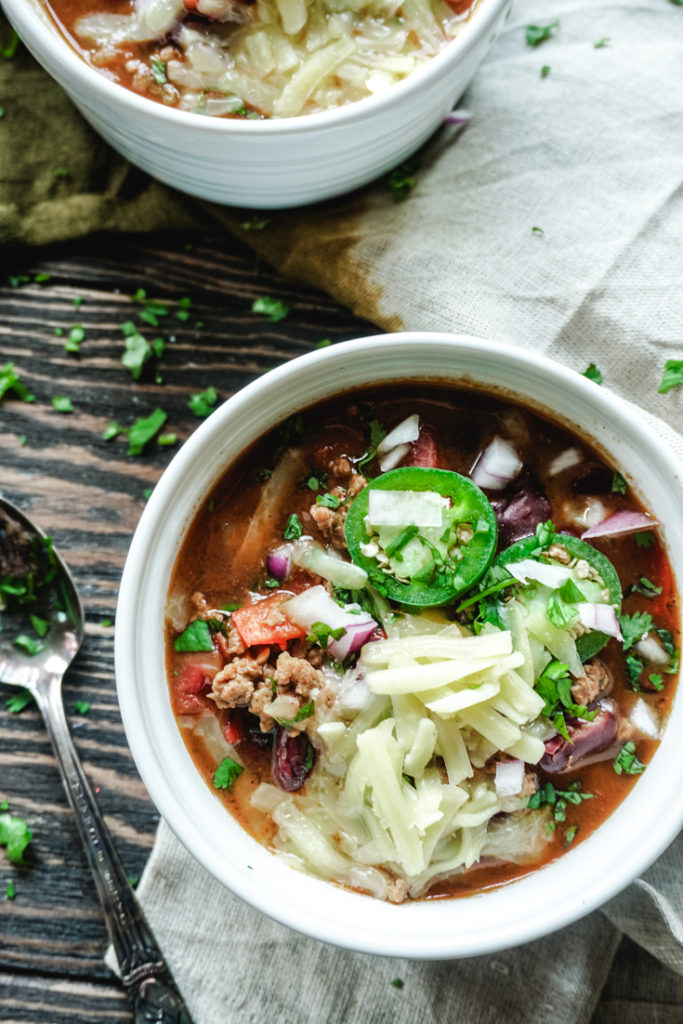 Turkey chili in a white bowl topped with cheese and jalapenos