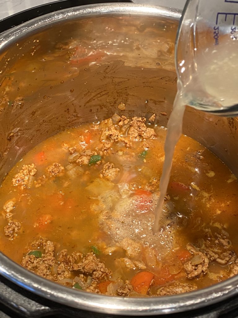 Stock being poured into an instant pot with ingredients for turkey chili in it