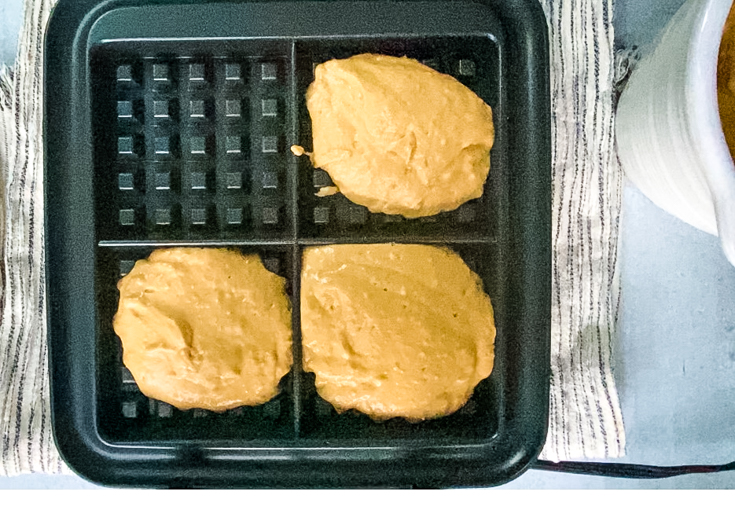 Waffle batter in three of the four compartments of a waffle iron