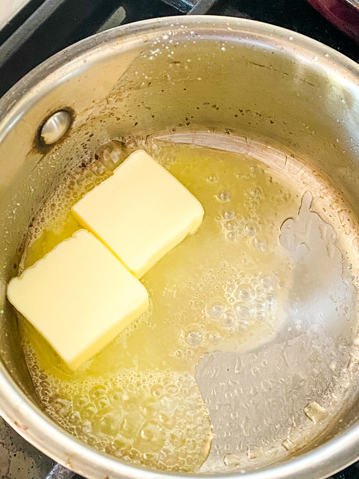 Two cubes of butter melting in a stainless steel saucepan