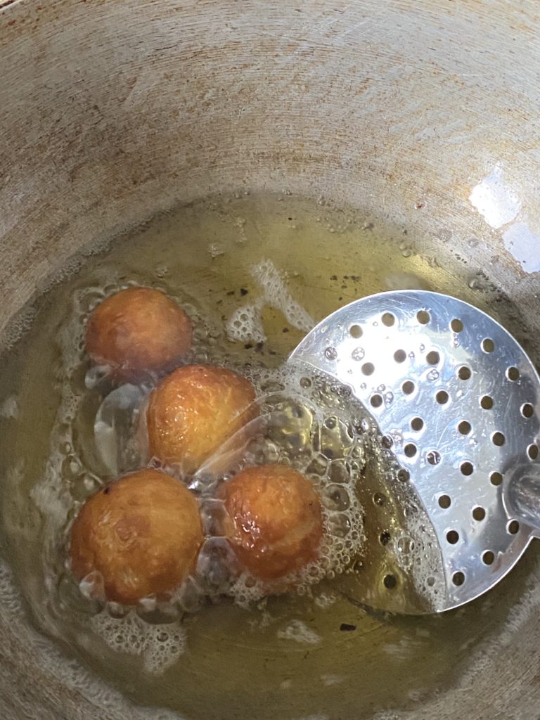 a ladle pushing the gulab jamun balls in oil