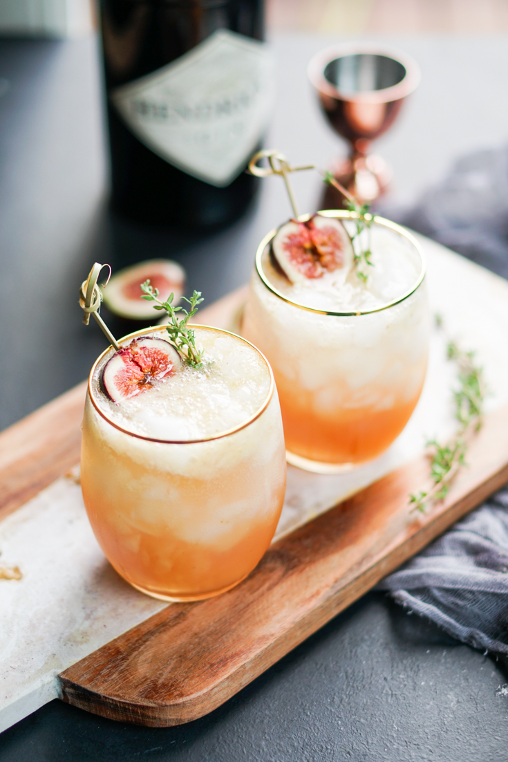 Two glasses with cocktails on a paddle board with figs around it