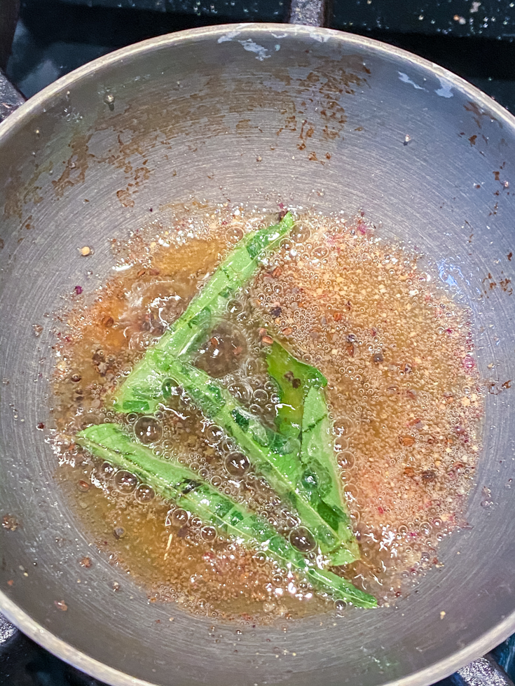 small pan with oil, spices and curry leaves in it