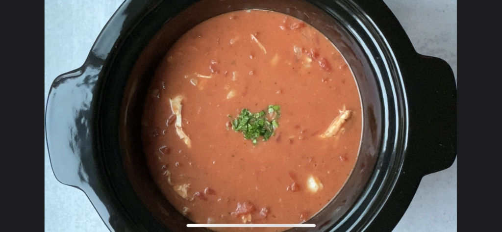 tomato chicken soup with basil on top in crockpot