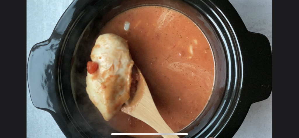 Wooden ladle scooping out a chicken breast from the crockpot