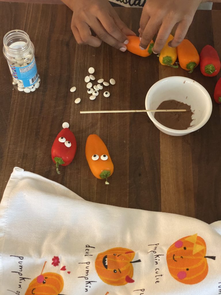 kids hand sticking candy eyes on peppers