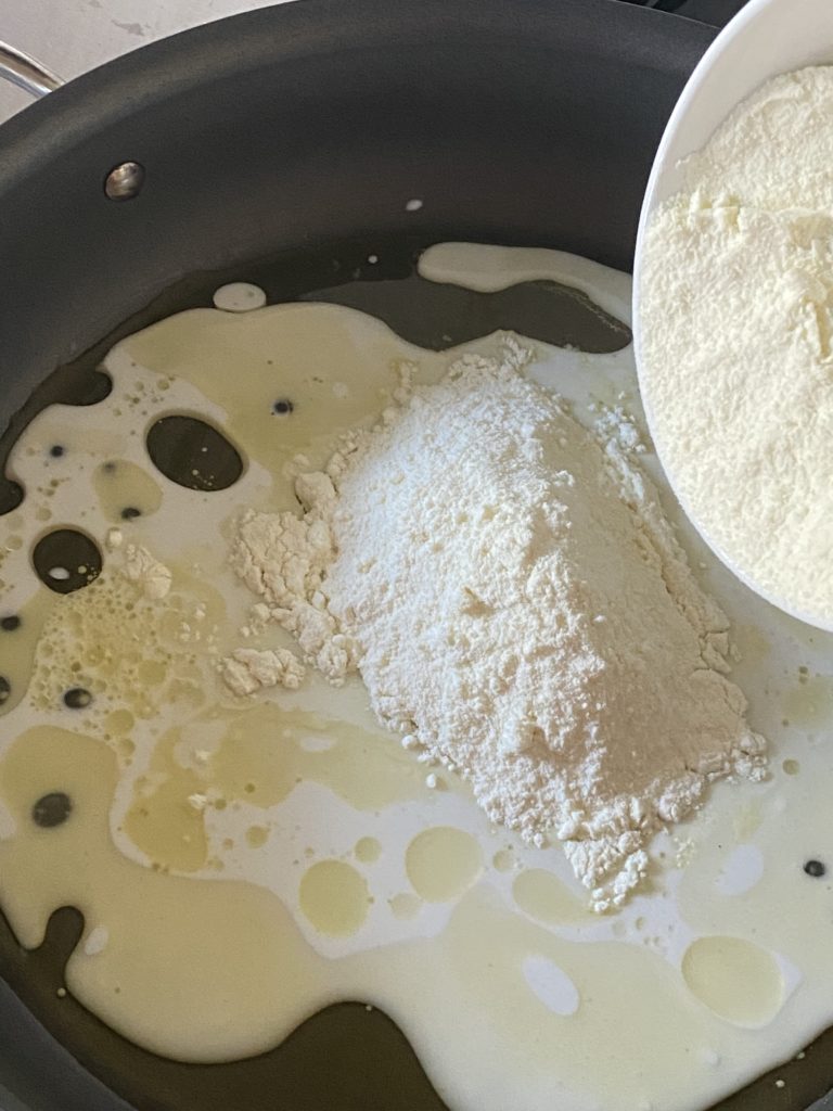 Milk powder being poured into a pan with milk in it