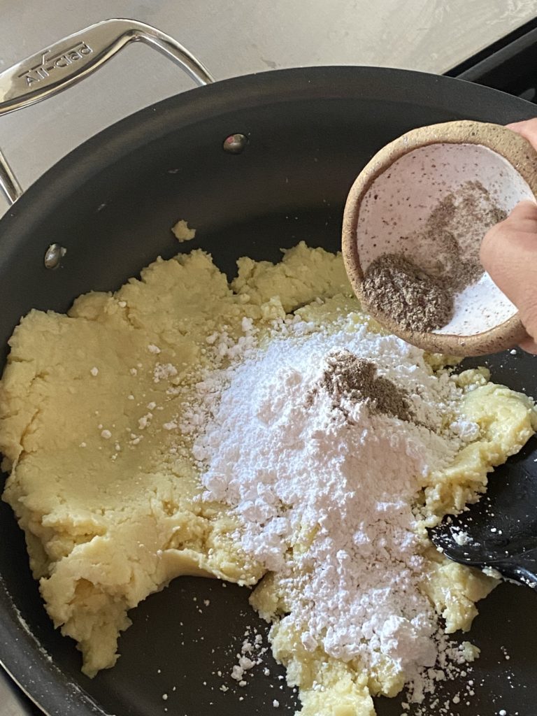 ground cardamom added to powdered sugar on milk powder mixture