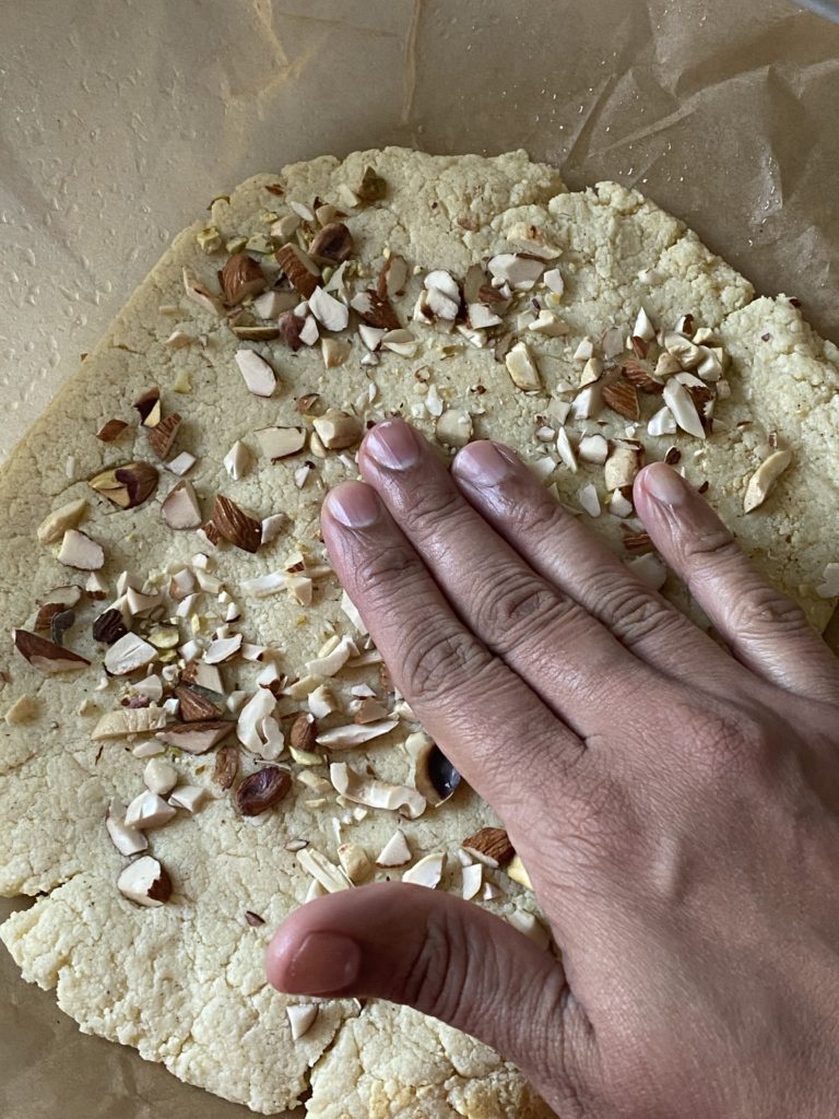 hand pressing down chopped mixed nuts onto the burfi