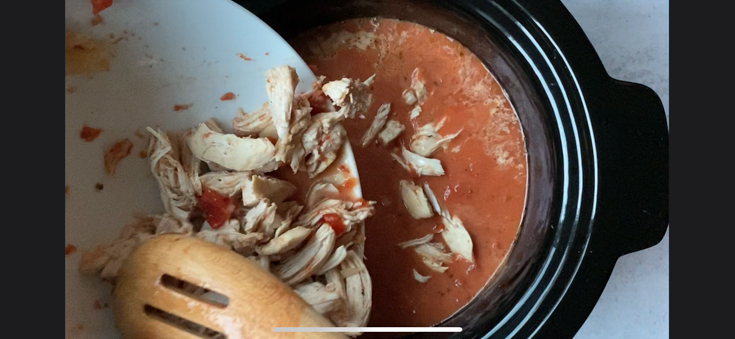 Shredded chicken being added to a tomato sauce base in a crockpot