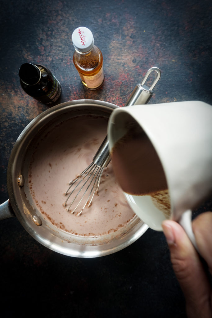 hand pouring nutella into a saucepan with hot chocolate