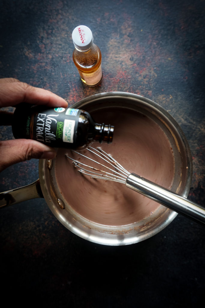Vanilla extract being poured into hot chocolate in a saucepan
