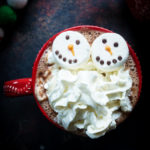 Hot chocolate topped with snowman marshmallows and whipped cream