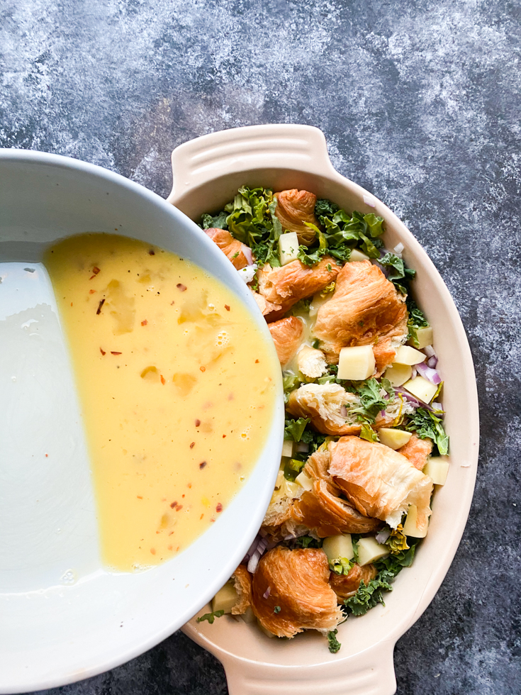 custard being poured into casserole dish with croissant and veggies in it