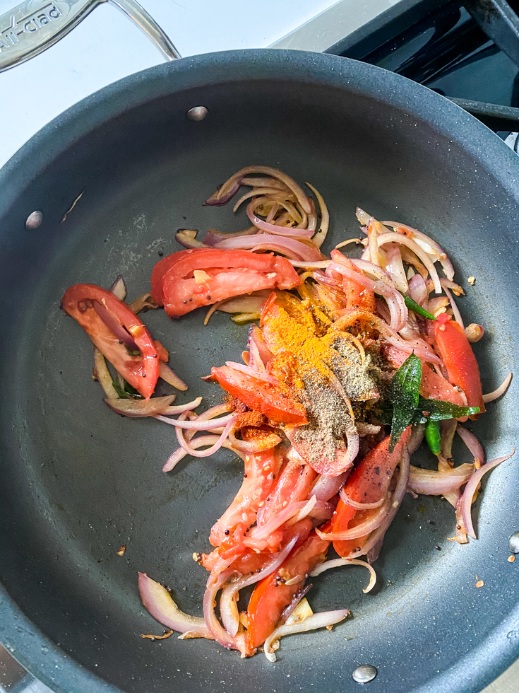 spices added on top of onions and tomatoes in a saute pan