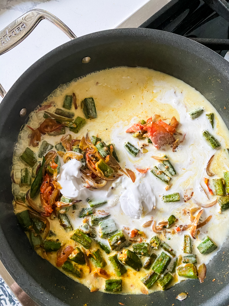 coconut milk poured into okra and veggies in a pan