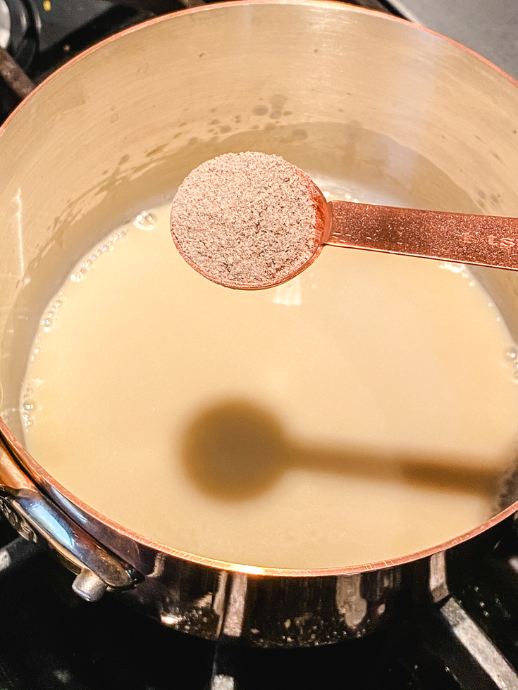 ground cardamom being added to coconut milk and jaggery in a saucepan
