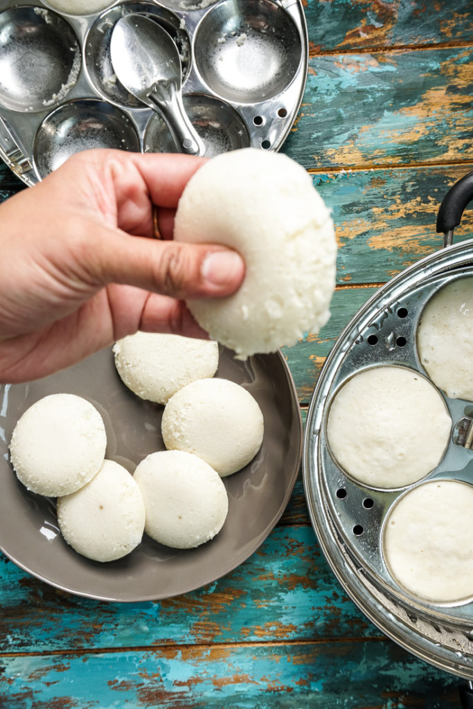 hand holding idli to show how fluffy it is