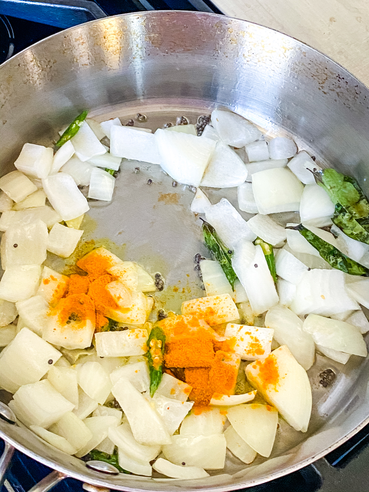 onions topped with turmeric powder in a saute pan