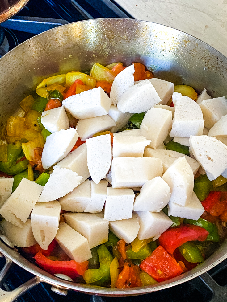 cut up idli pieces on top of veggies in a saute pan