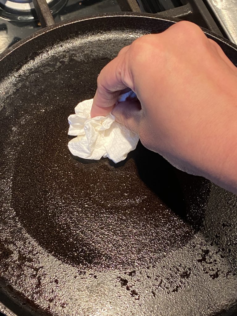 hand spreading oil on a griddle with a paper towel