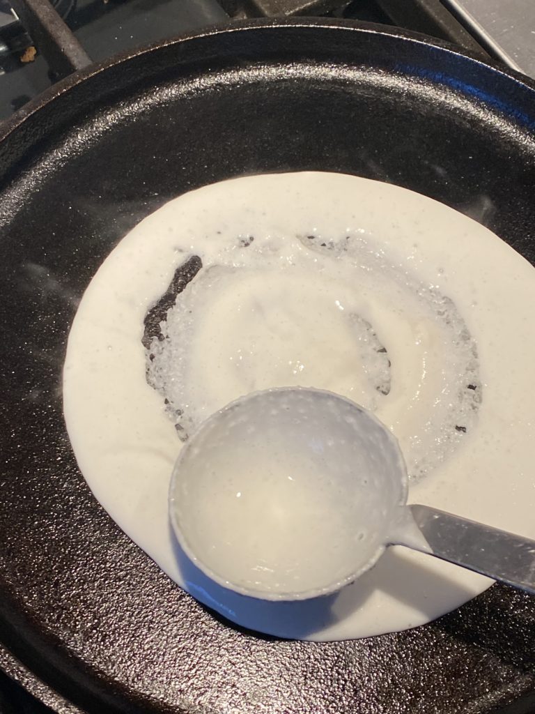 ladle spreading dosa batter on griddle