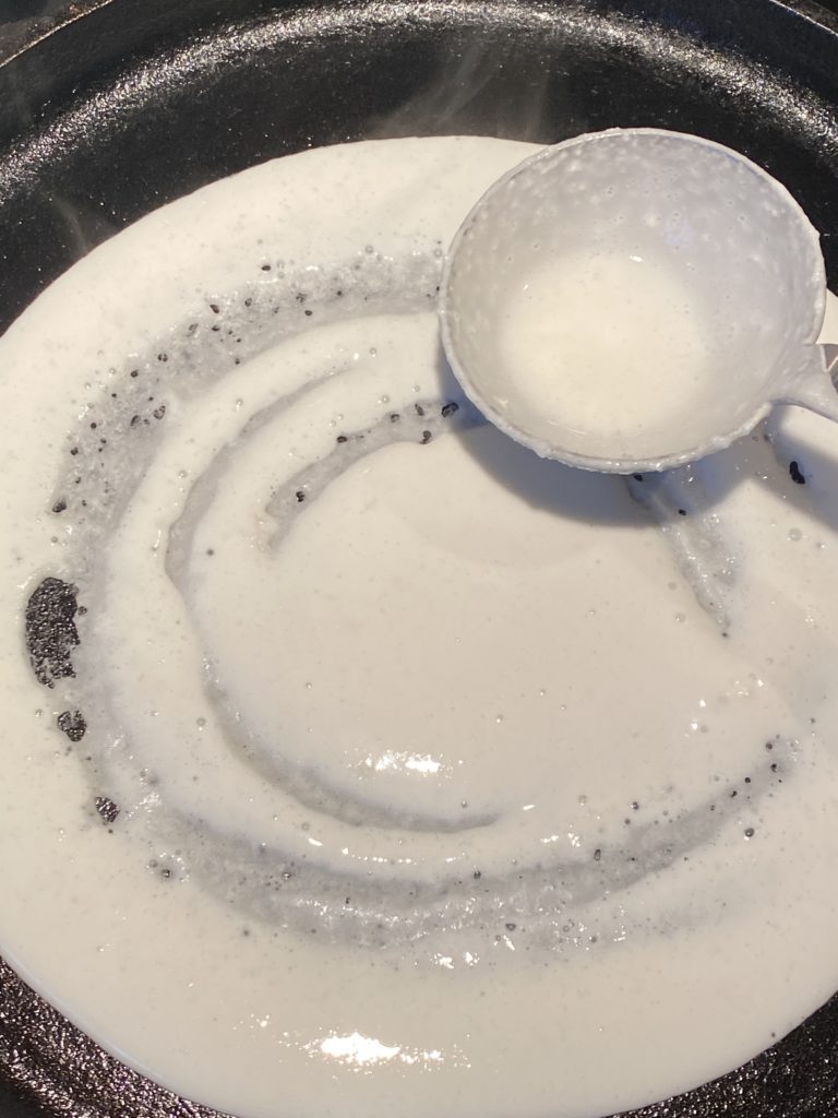 ladle spreading dosa batter on griddle