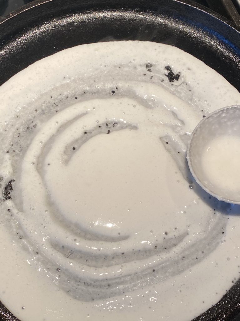 ladle spreading dosa batter on griddle