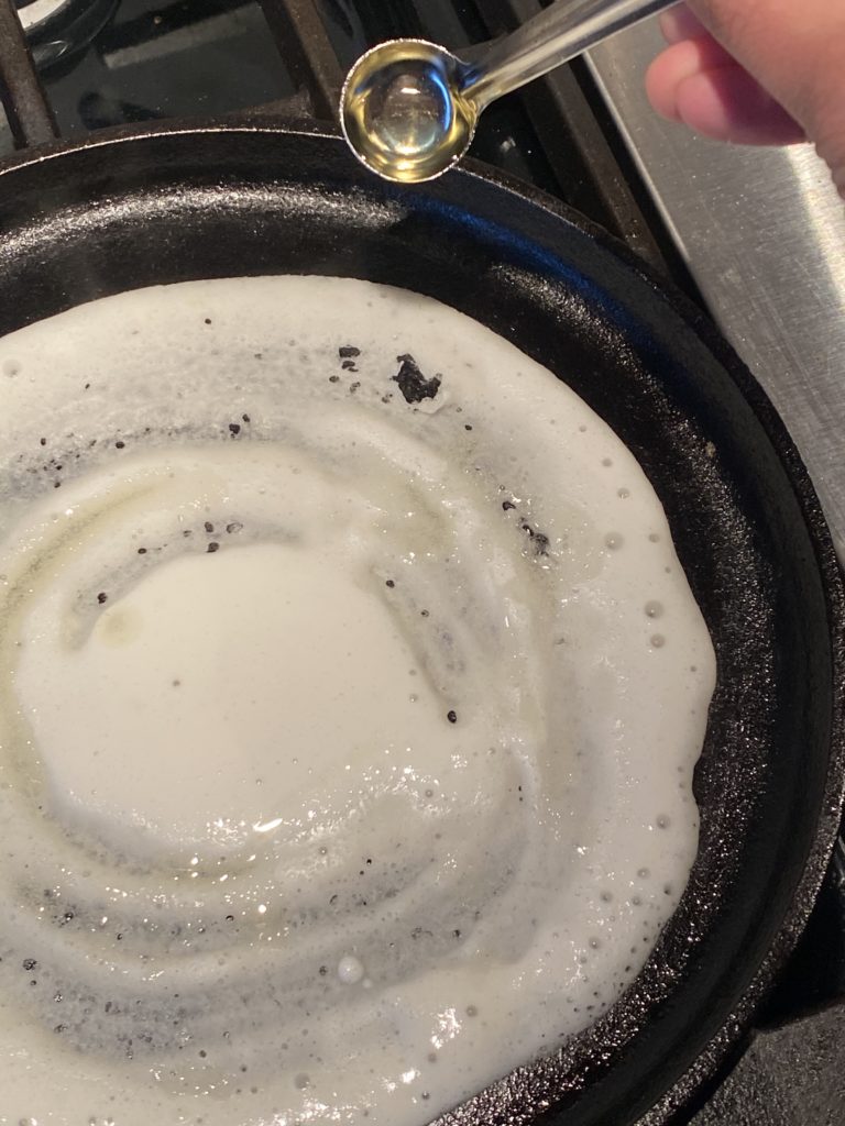 oil being poured on the dosa on a griddle