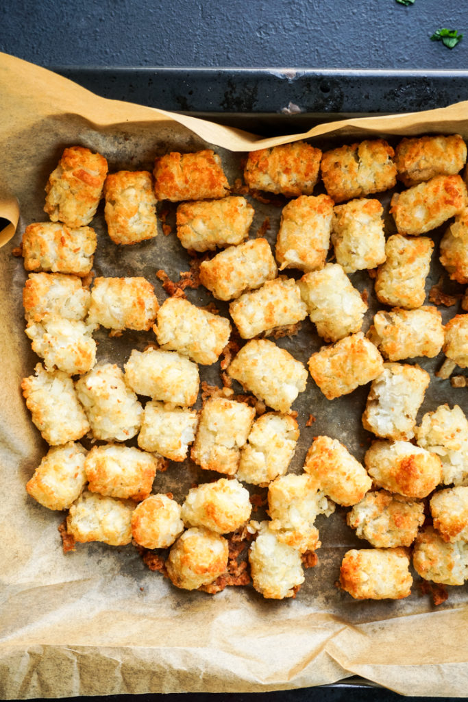 cooked tater tots in parchment lined baking sheet