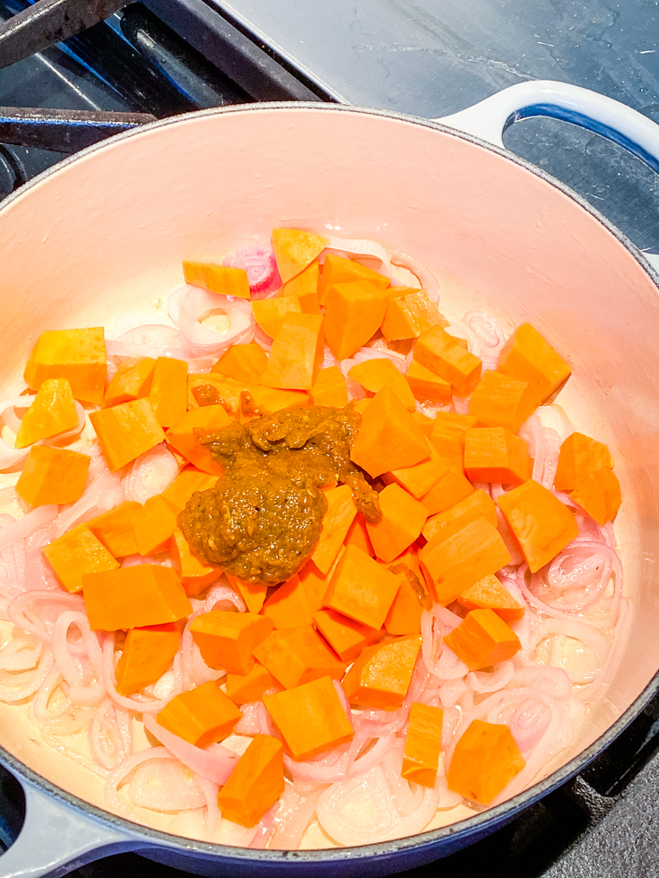 Onions and sweet potatoes topped with Thai red curry paste in a Dutch oven