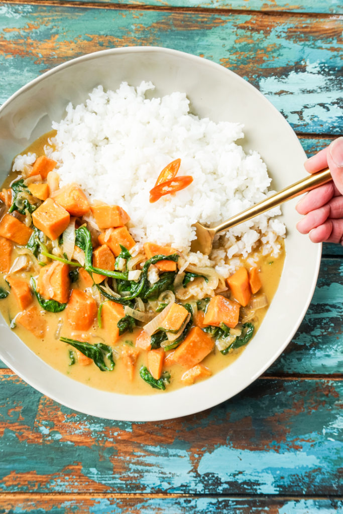 Thai sweet potato curry and white rice in a bowl with a gold fork