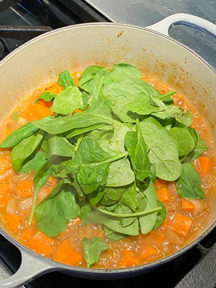 Baby spinach added to a pot of cooked sweet potatoes