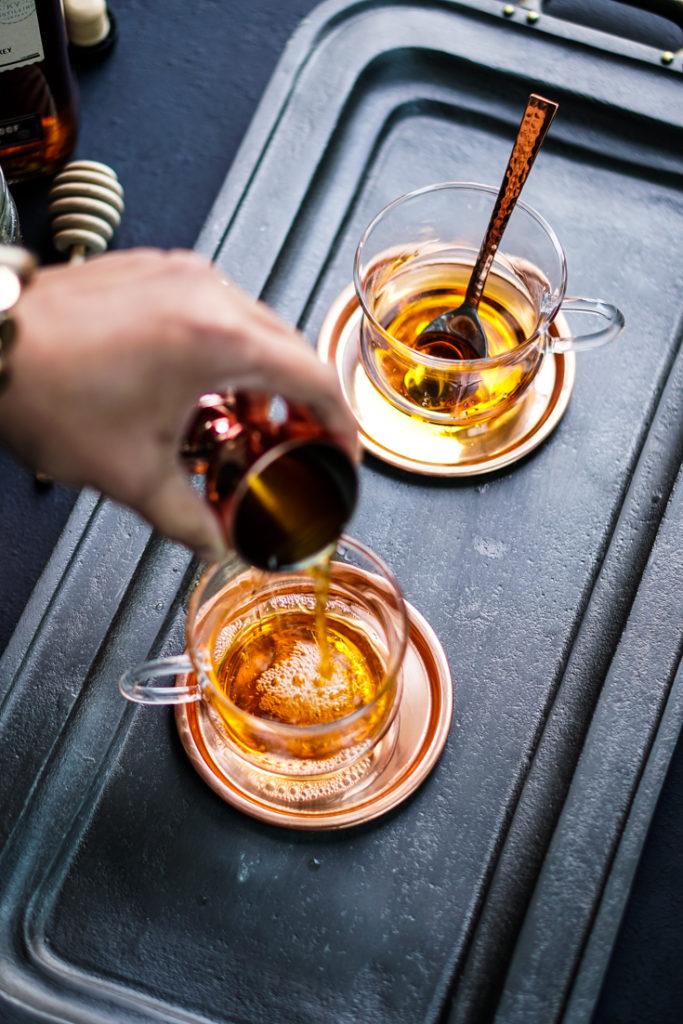 hand pouring bourbon into a glass cup