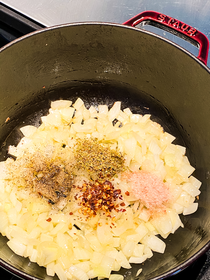 Dried oregano, salt, pepper, red pepper flakes added to onions in a Dutch oven