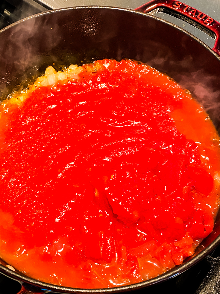 canned tomatoes added to onions in a Dutch oven