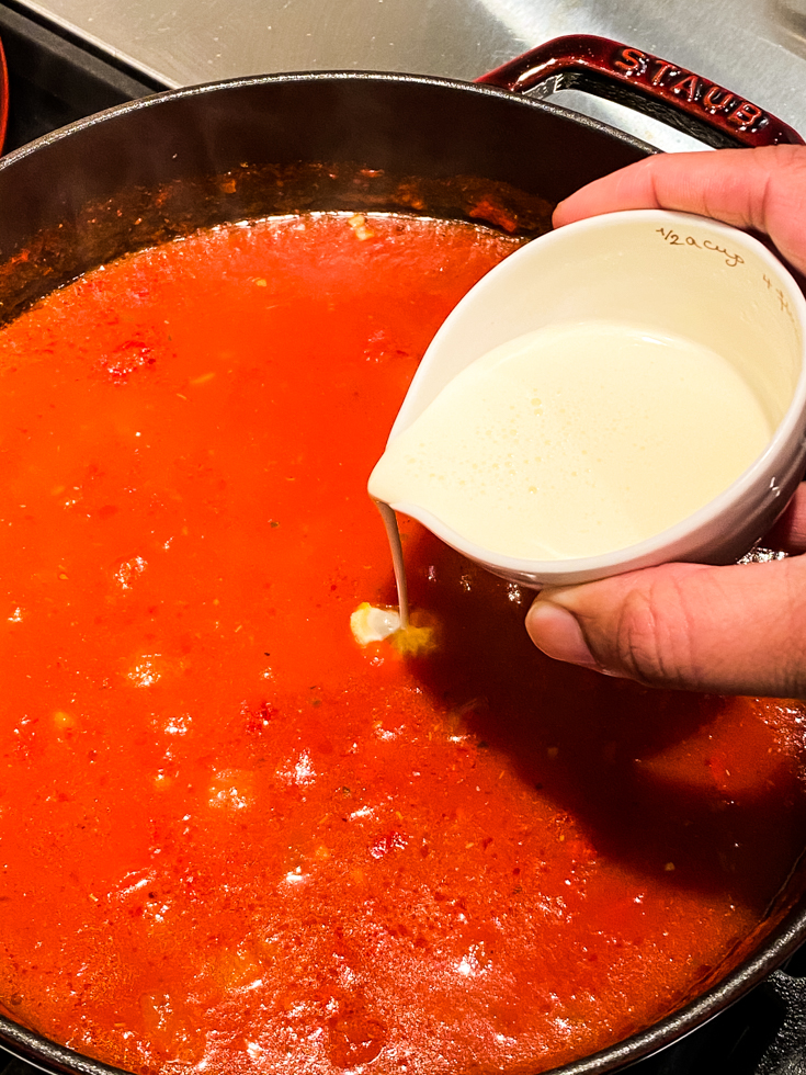 cream being added to a Dutch oven with tomato soup in it