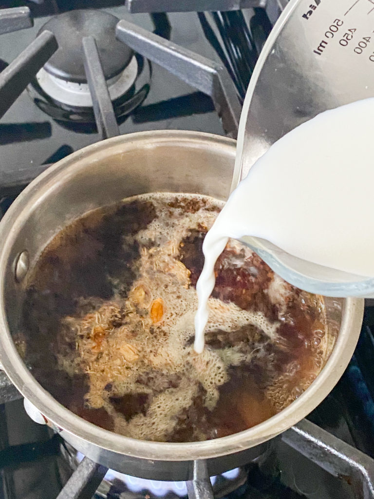 milk being added to a saucepan with water and tea leaves in it