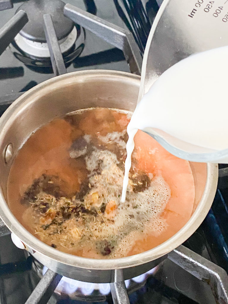 milk being added to a saucepan with water and tea leaves in it