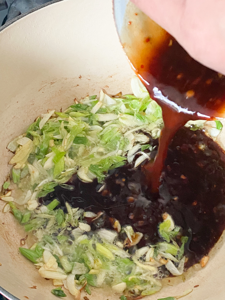 sauce being poured into pan with scallions