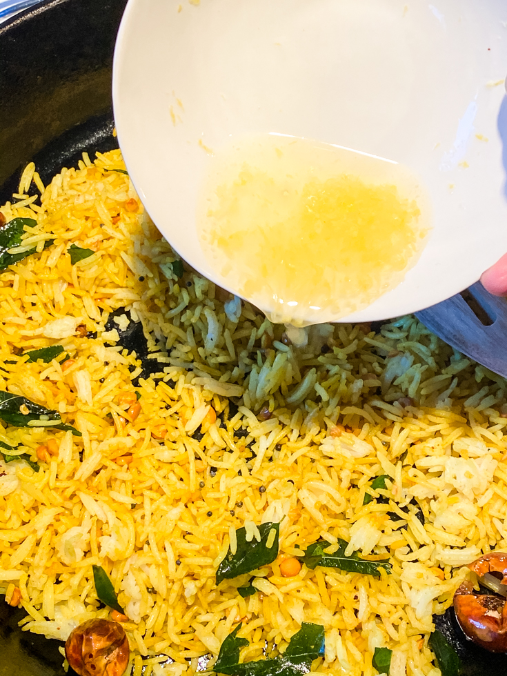 lemon juice and zest being poured over rice in a skillet
