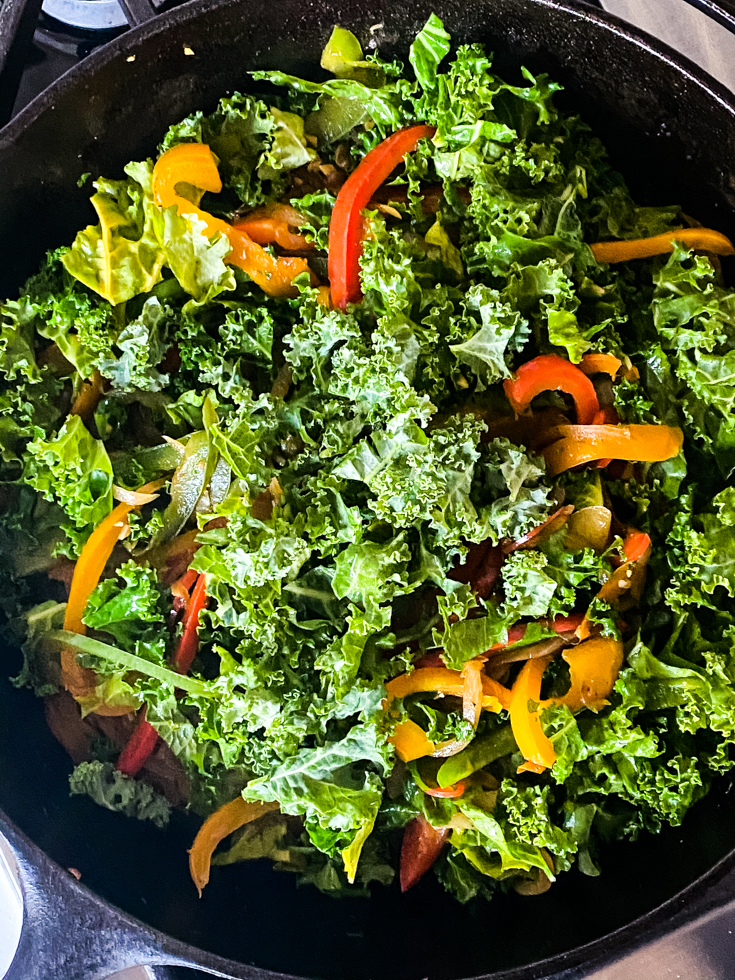 kale on top of peppers in a skillet