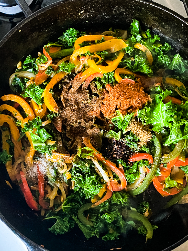 spices on top of kale and peppers in skillet