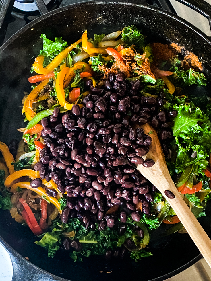 black beans added to skillet with peppers and kale in it