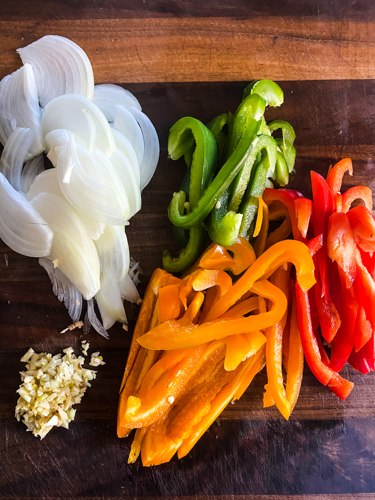 sliced onions, peppers and minced garlic on a cutting board
