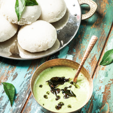 a copper bowl of cilantro coconut chutney with a plate of idlis on the side
