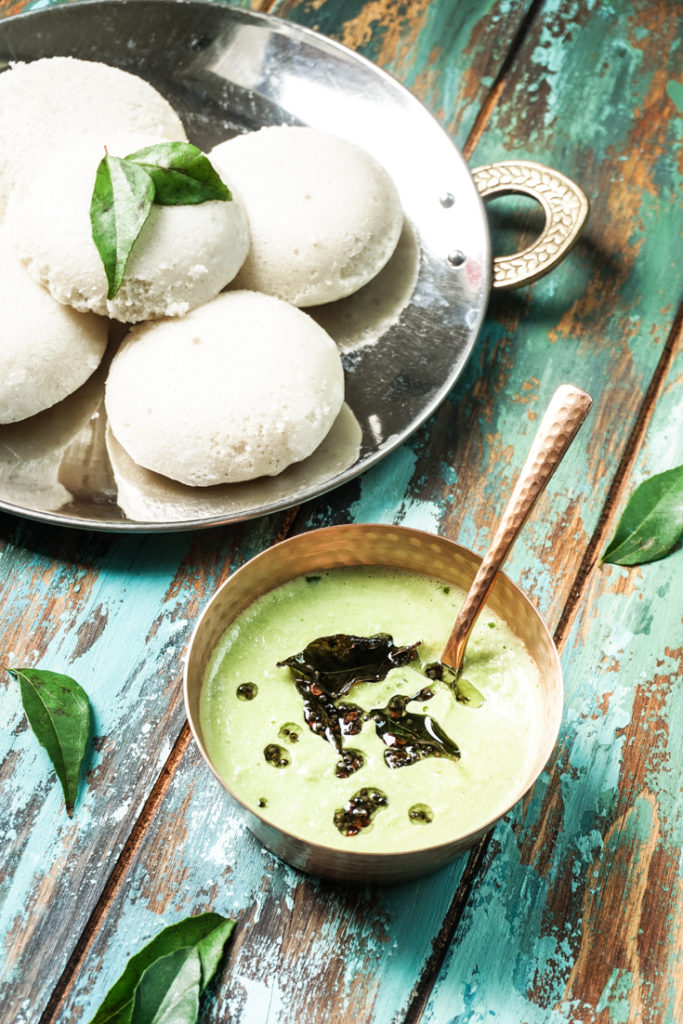 a copper bowl of cilantro coconut chutney with a plate of idlis on the side