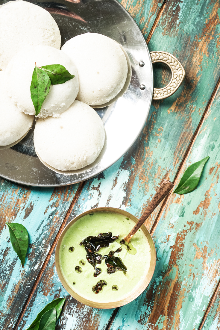 a copper bowl of cilantro coconut chutney with a plate of idlis on the side