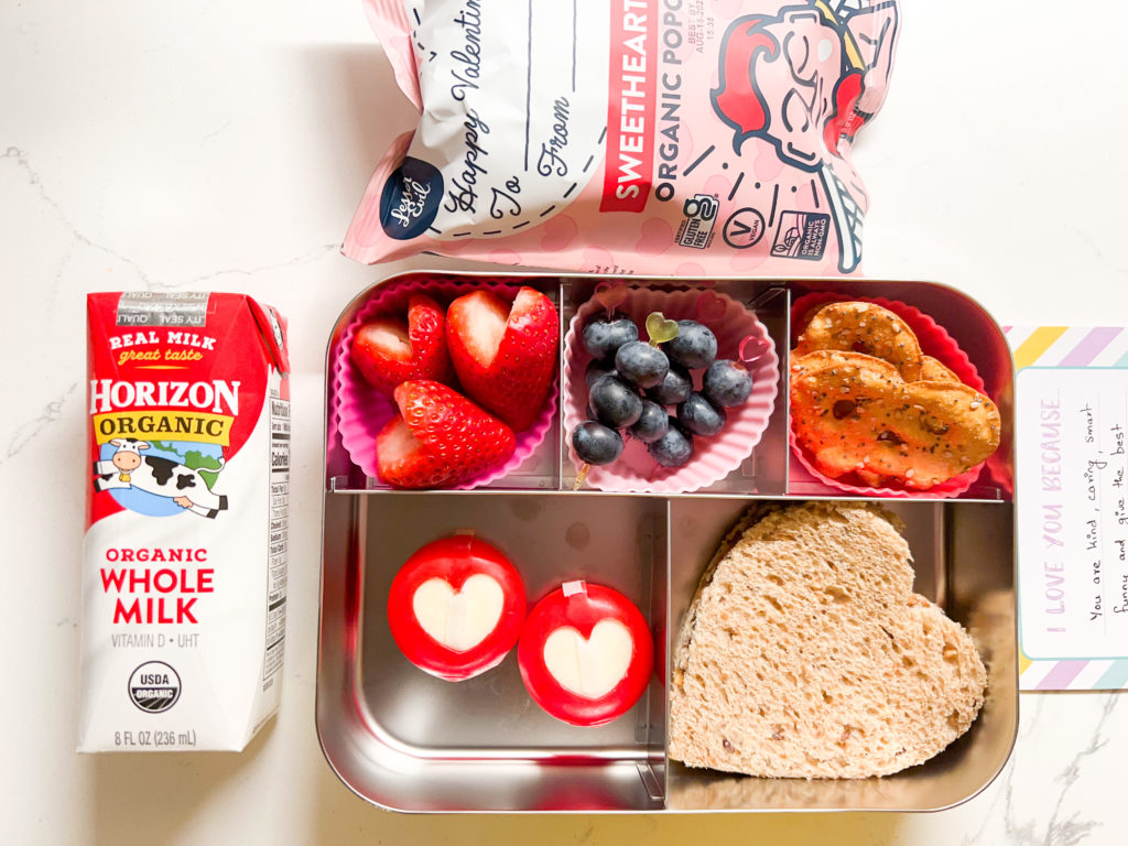 Kids lunch box with valentines themed food, milk box and a snack pack on the sde