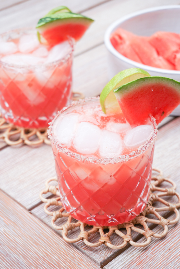 two glasses of watermelon margarita on the rocks with lime wedges